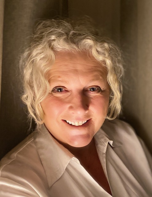 A white-blonde woman with blue eyes is smiling at the camera.